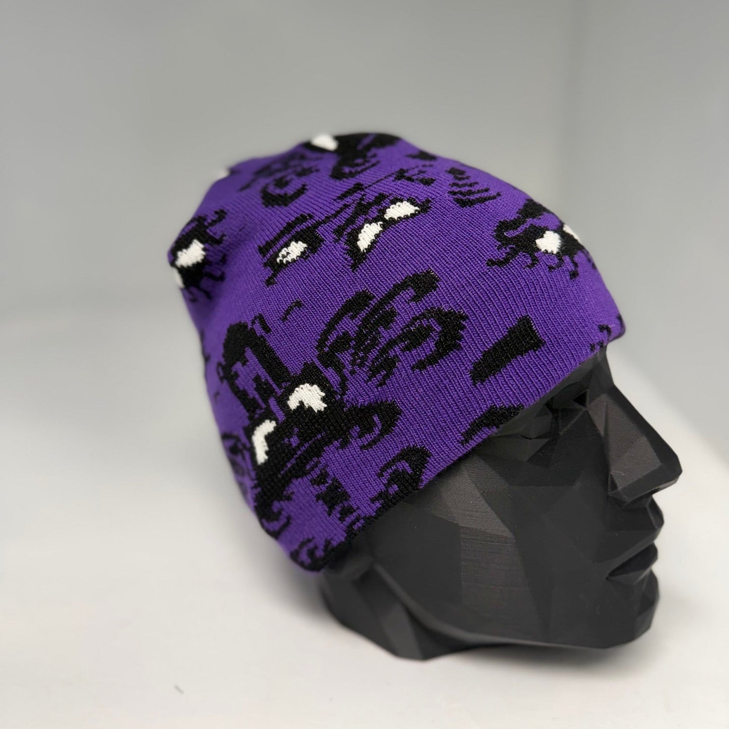 Purple beanie with black cat pattern on a mannequin head against a gray background