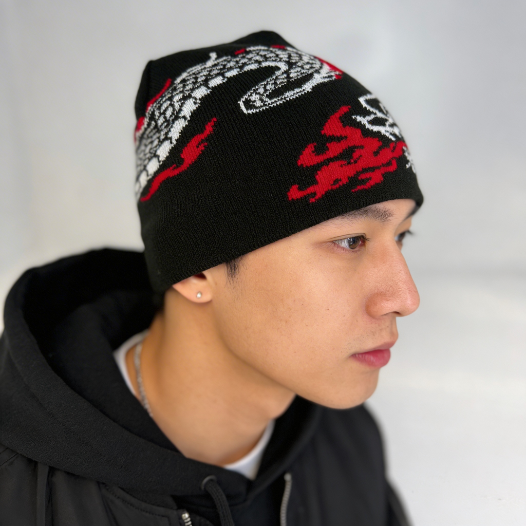 Person wearing a black beanie with red and white designs on a plain background