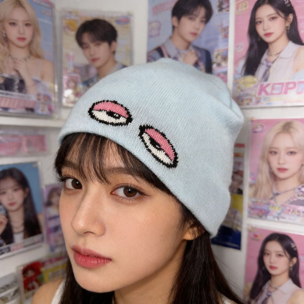 Person wearing a light blue beanie with decorative elements in front of a collage of photos