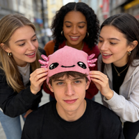 Three friends adjusting a pink hat with cartoon face design on a city street.