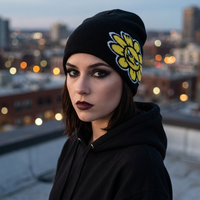 Person wearing a black beanie with a yellow flower design, standing on a rooftop with city lights in the background.