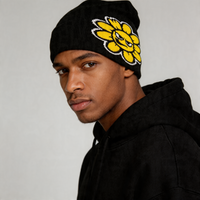 Person wearing a black beanie with a yellow flower design on a gray background