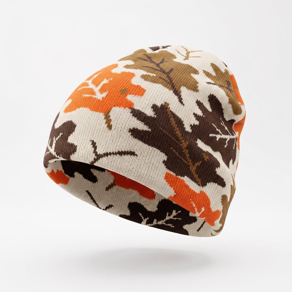 A knit beanie hat featuring an autumn leaf pattern in orange, brown, and dark brown on a cream background, shown floating against a light gray studio background.
