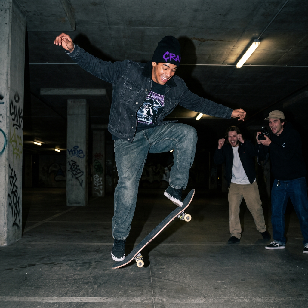 Skateboarder performing a trick in an underground setting with onlookers.