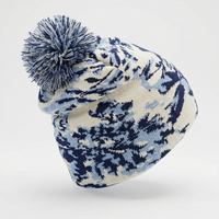 Knitted beanie with blue and white pattern and pom-pom on a light gray background