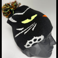Black knit beanie with colorful pom-pom on a mannequin head against a white background