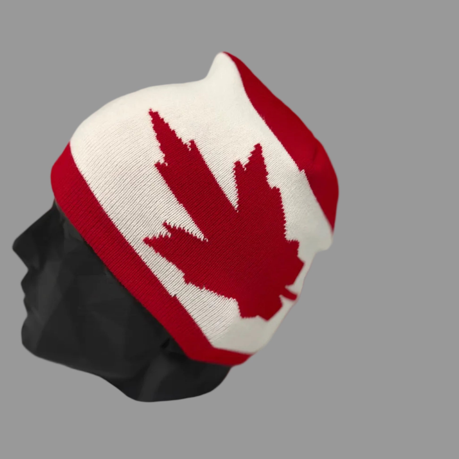 White beanie with red maple leaf design on a mannequin head against a gray background