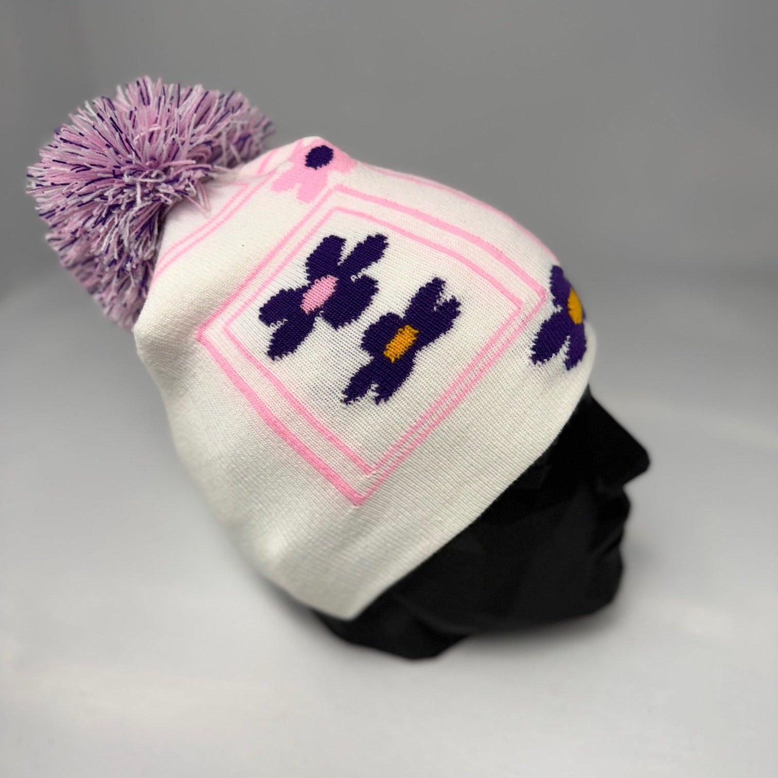 White beanie with pink diamond pattern and purple flowers on a gray background