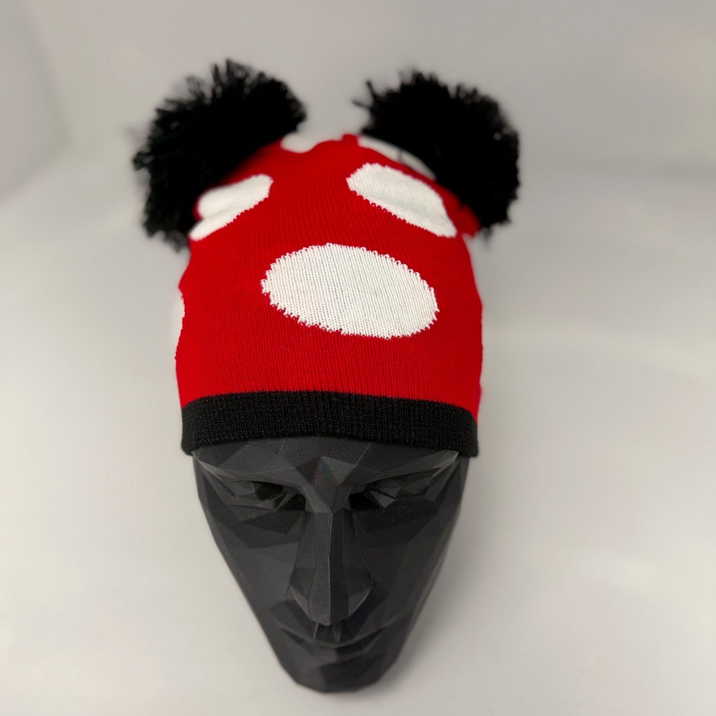 Red and black knitted hat with white polka dots on a mannequin head against a white background