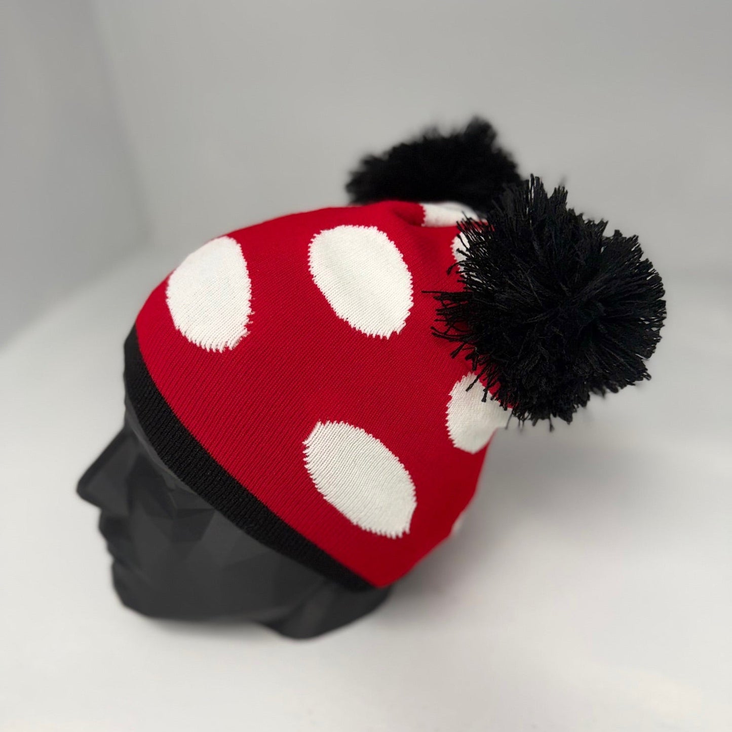 Red and white polka dot beanie with a black pom-pom on a mannequin head against a gray background