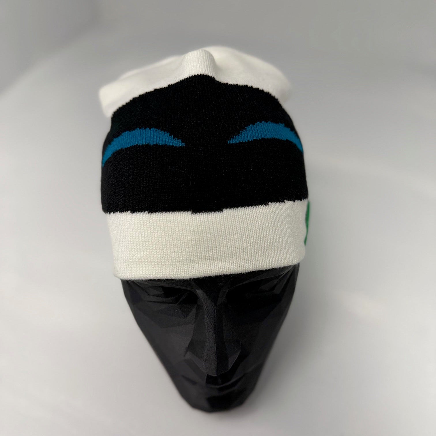 Knitted beanie with black, white, and blue pattern on a mannequin head against a gray background