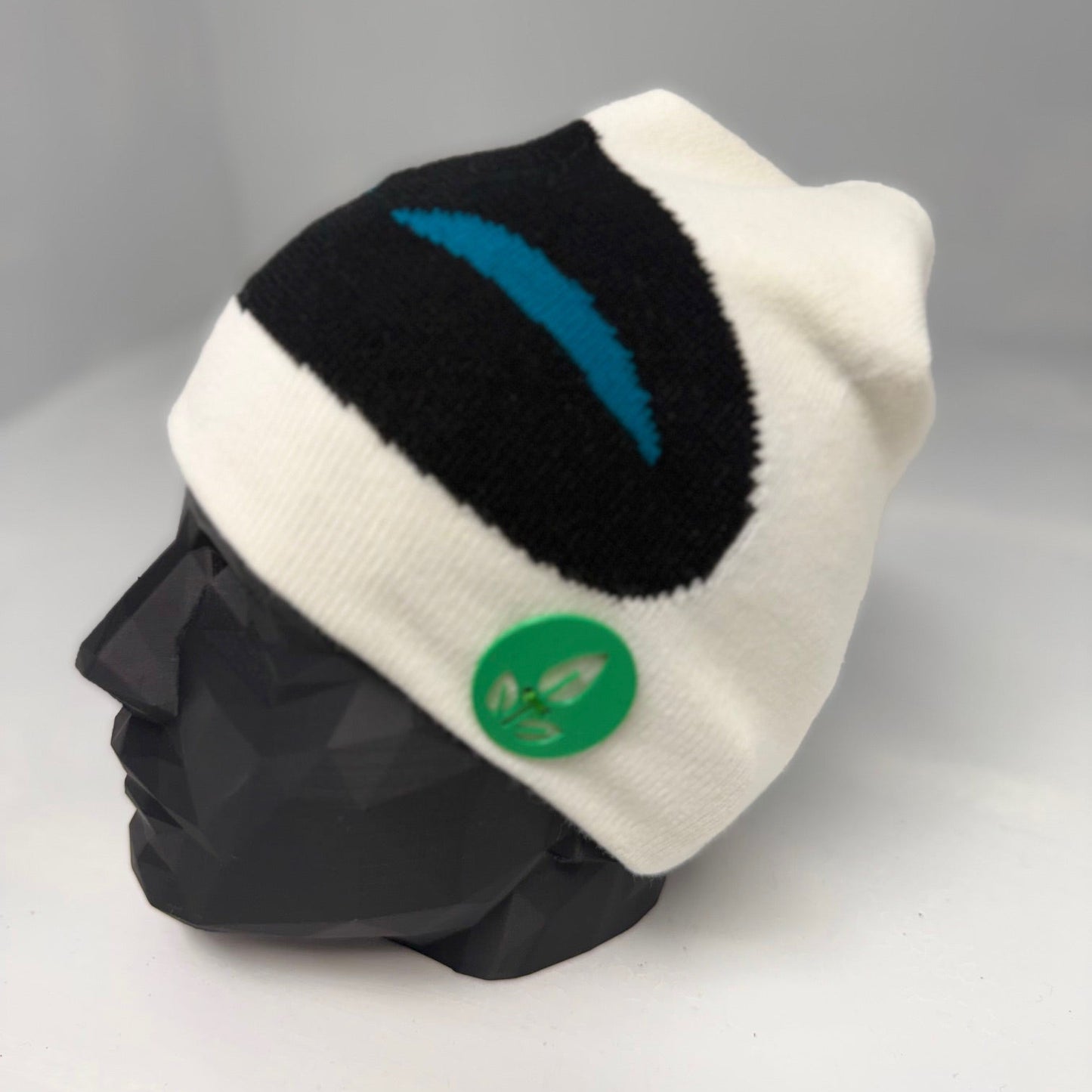 White and black beanie with a green logo on a mannequin head against a gray background
