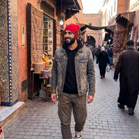 Man walking through a bustling market street with shops and people in the background.
