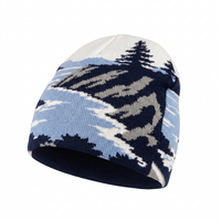 A knit beanie hat featuring a mountain and pine tree pattern in navy blue, light blue, gray, and off-white, shown on a plain white background.