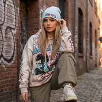 Woman wearing a graphic hoodie and beanie in an urban setting with graffiti.