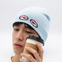 Person wearing a light blue beanie with pixelated lips design, holding a coffee cup.