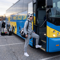 Person boarding a blue and yellow bus with 'City Women's Soccer Team' branding.