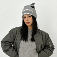 Woman wearing a gray dress, jacket, and shark hat against a white background