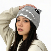 Person wearing a gray beanie with a shark mouth design and a beige hoodie with black text.