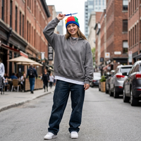 Person wearing a colorful beanie and gray hoodie on a city street.
