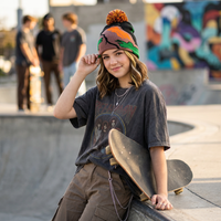 Person sitting with a skateboard at a skate park, wearing a colorful beanie and graphic t-shirt.