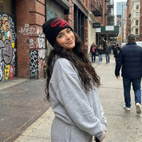 Woman wearing a gray sweatshirt and black beanie with red design on a city street.
