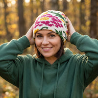 Woman wearing a colorful patterned beanie and green hoodie in a forest setting