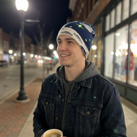 Man wearing a blue and white beanie with green stars on a city street at night.