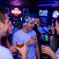 People socializing in a bar with drinks and neon signs.