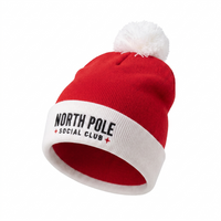 A red knit pom-pom beanie with a white cuff featuring the text 'NORTH POLE SOCIAL CLUB' in black and small red star accents, shown on a plain white background.