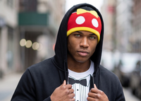 Person wearing a black hoodie with a mickey mouse beanie standing on a city street.
